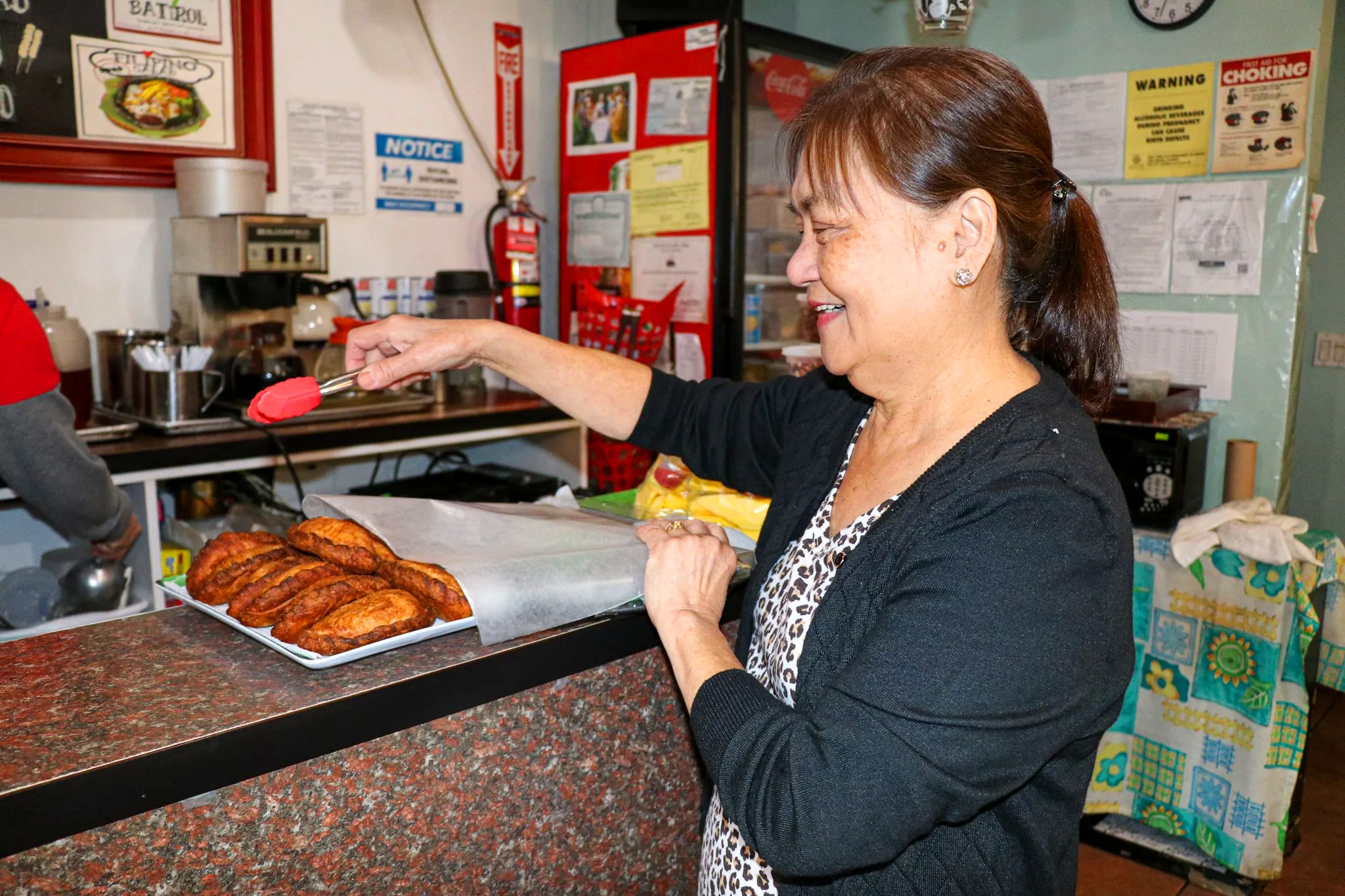 A woman leans over a counter selecting a turnover with tongs.