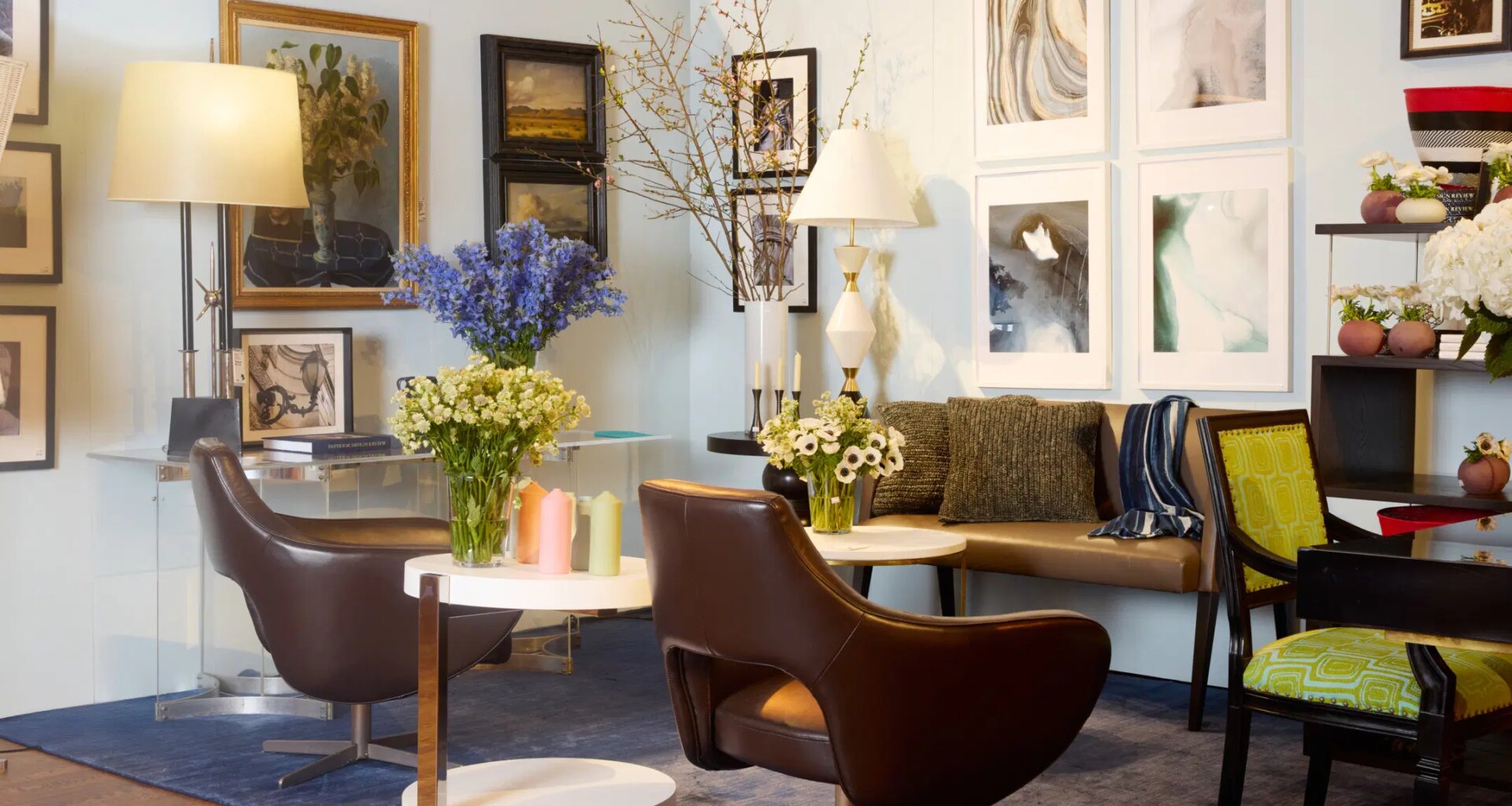 Modern living room with art on walls, brown chairs, floral arrangements on tables, and mixed decor elements.