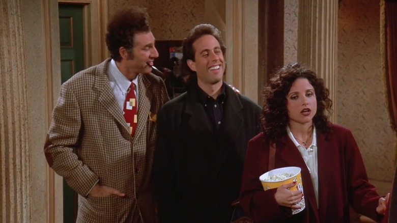 Kramer smoking a pipe, Jerry laughing, and Elaine holding a tub of popcorn in Seinfeld