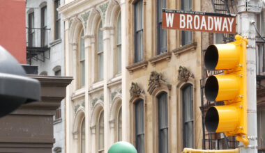 A close-up of a street sign reading W Broadway and a yellow traffic light, set against historic stone buildings with arched windows—capturing the charm of the Manhattan real estate market in an urban setting.
