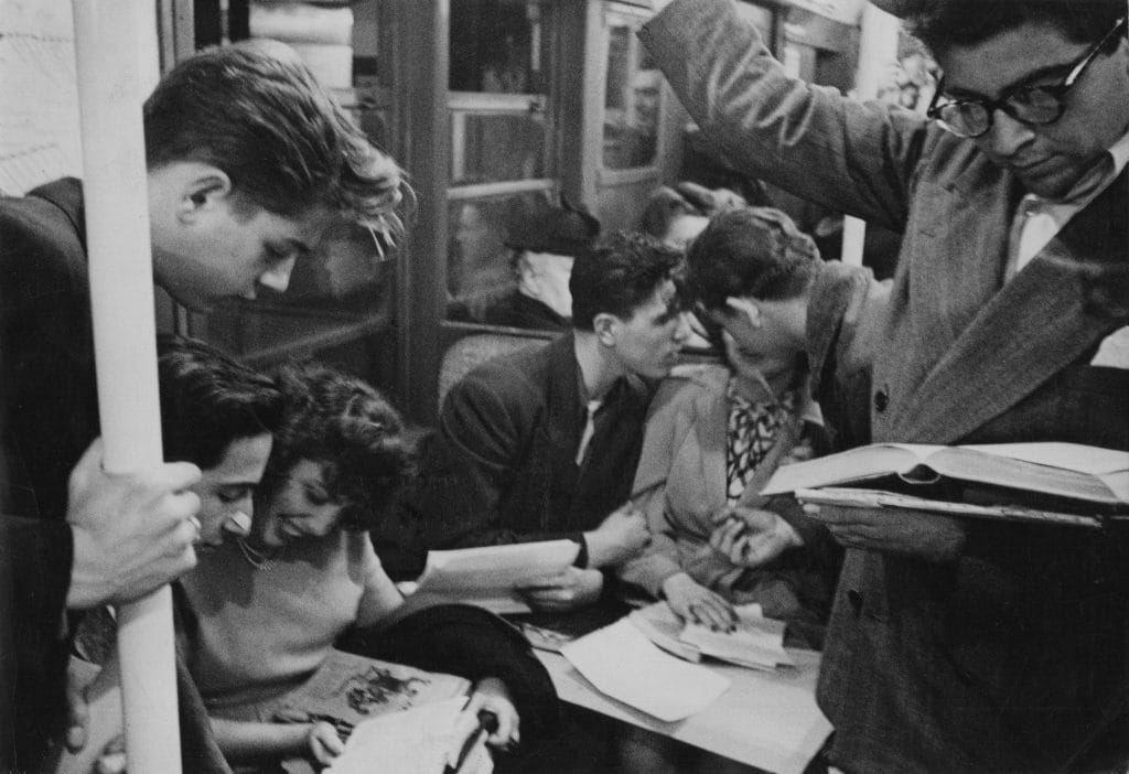 A black and white photo by Stanley Kubrick depicting a crowded subway train full of young men and women talking