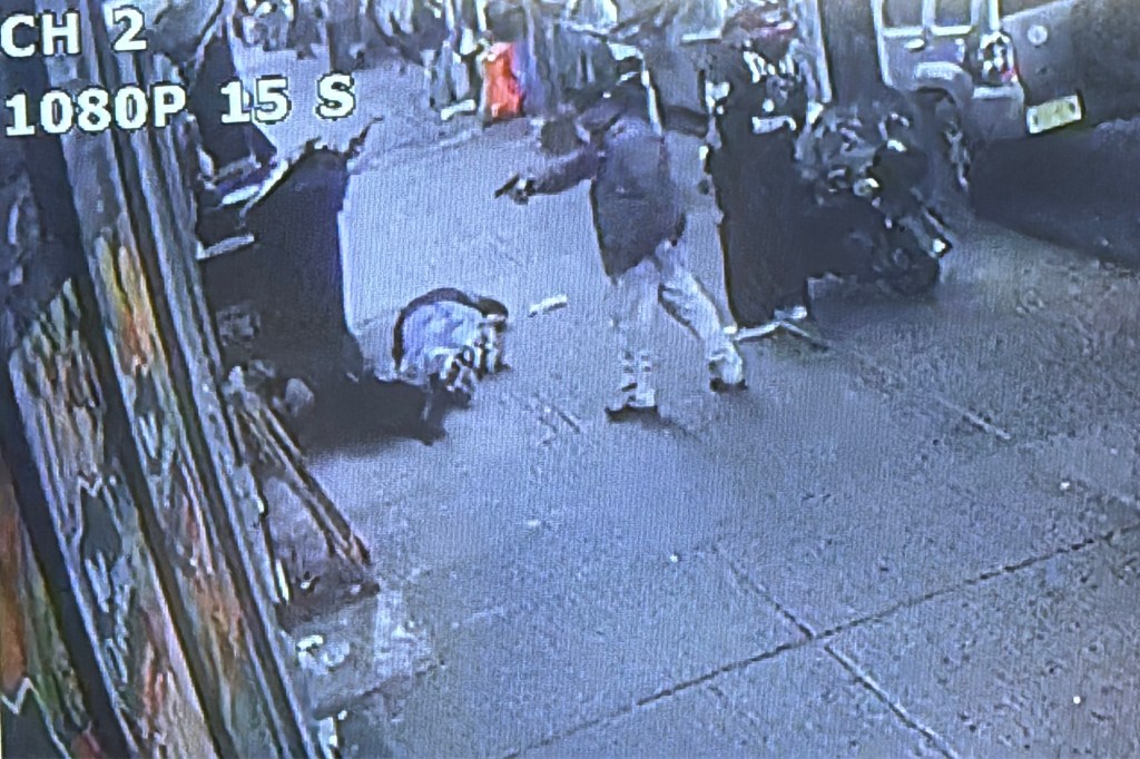 Surveillance video still showing a person pointing a gun at another person on the ground.