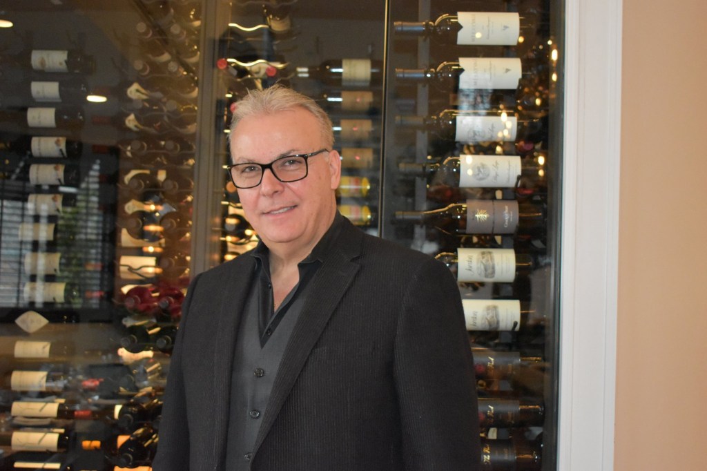 Stavros Aktipis, founder of Table To Table, standing in front of a wine rack.