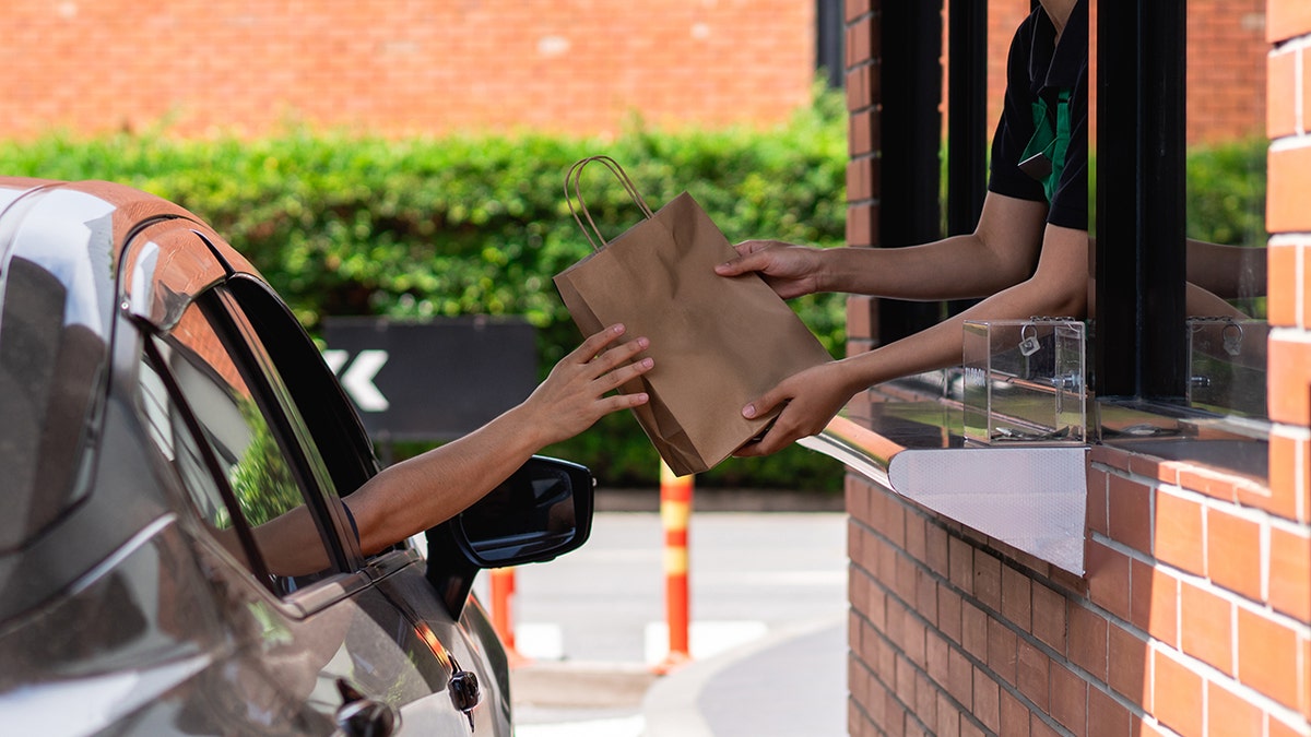 Person in car receiving bag from worker at fast-food drive-thru window