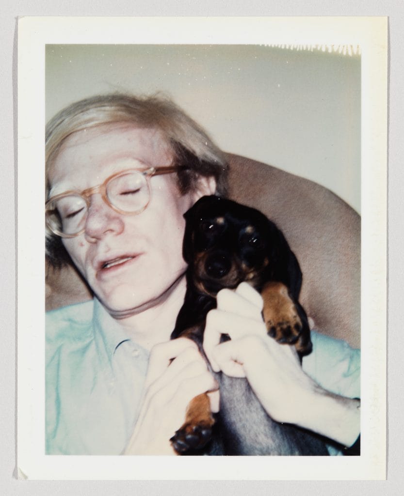 Polaroid photo of Andy Warhol cuddling in an armchair with his dog