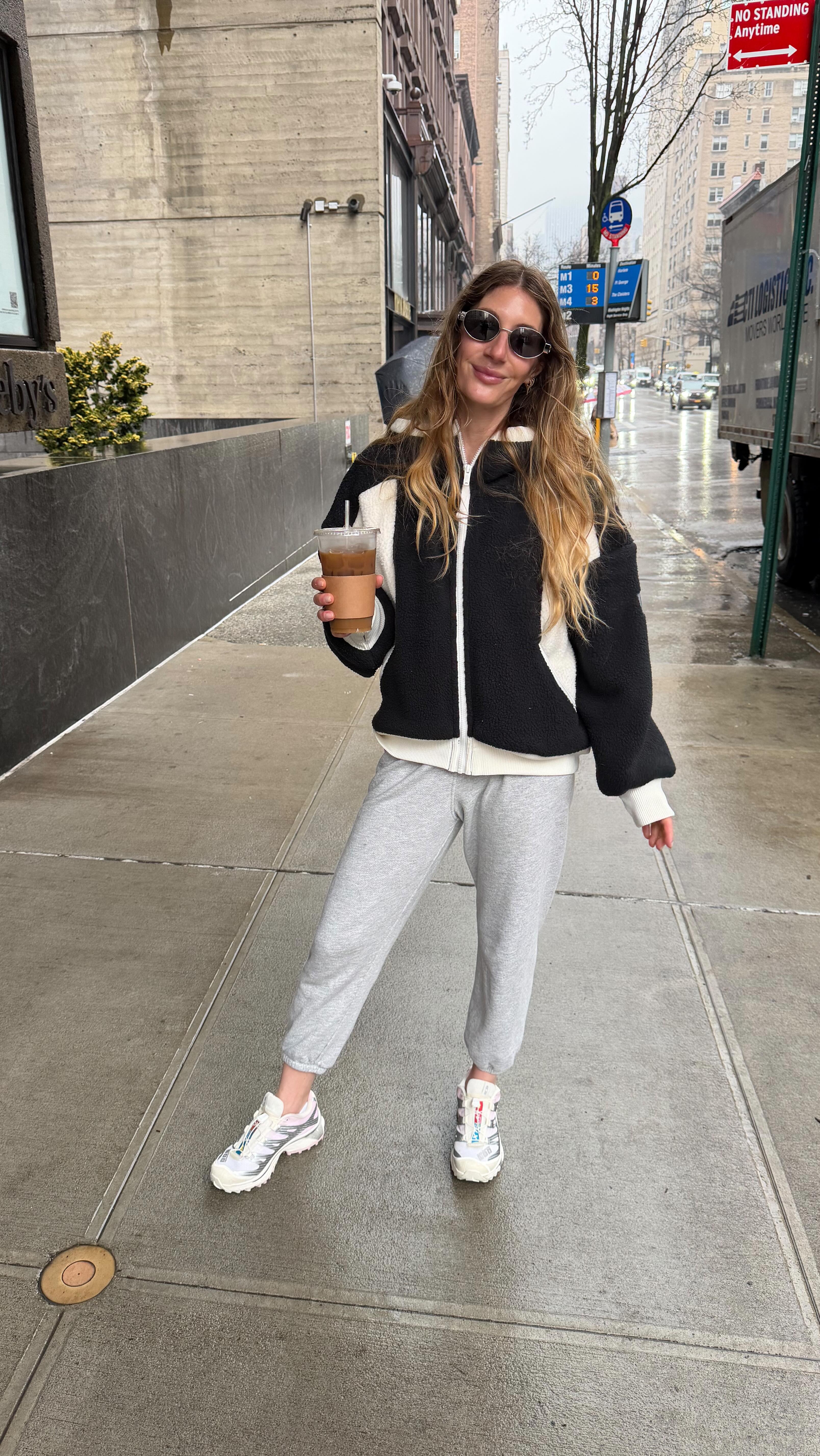 A woman wears gray sweatpants, a black sweater, and white salomon sneakers.