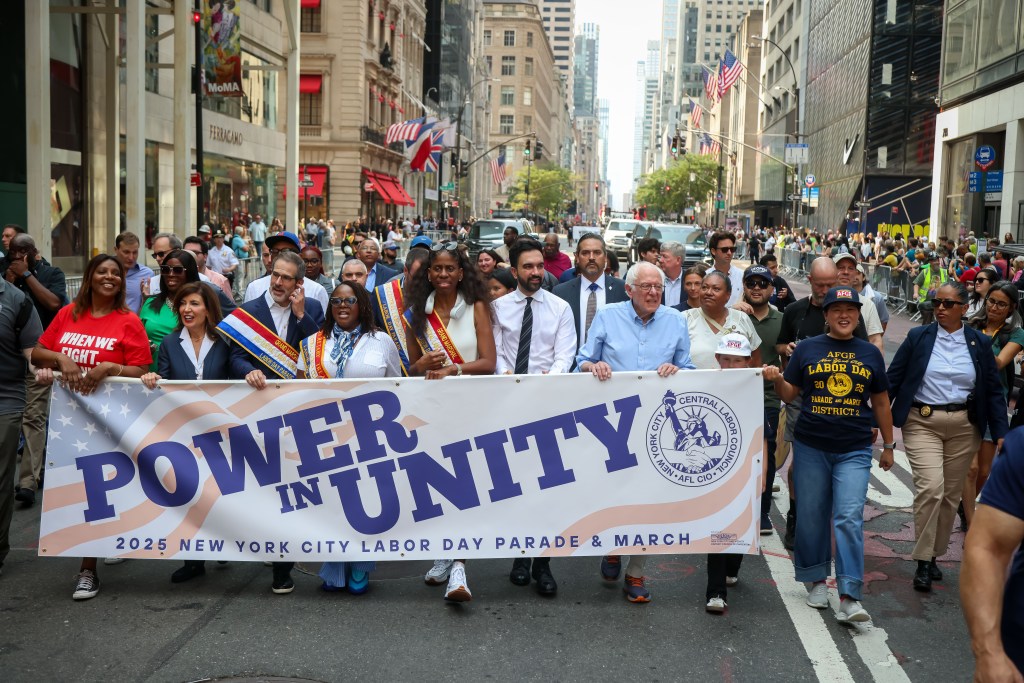 Zohran Mamdani and Bernie Sanders march in the 2025 NYC Labor Day Parade, holding a "POWER IN UNITY" banner.