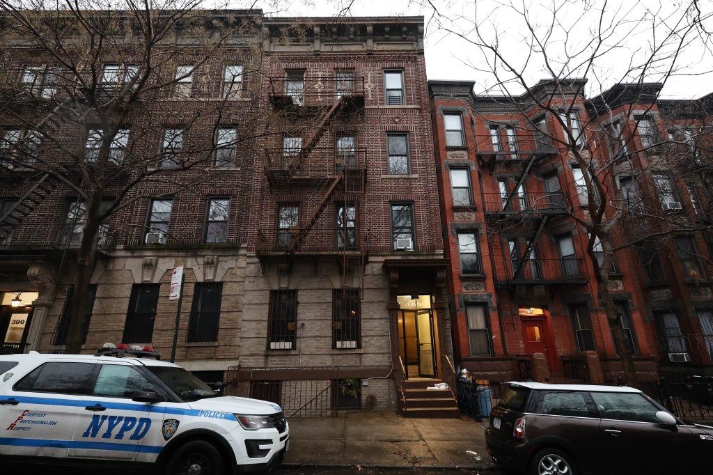 An NYPD police car is parked in front of brick apartment buildings.