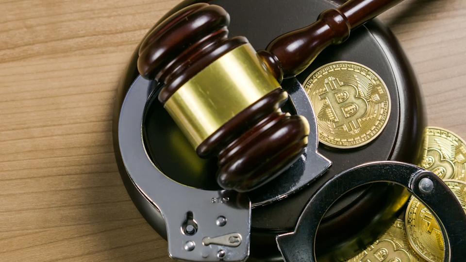 A judge's gavel pictured with handcuffs and gold coins strewn about