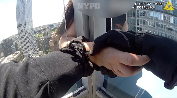 A responding NYPD officer holds the hand of a distraught woman seated on the ledge of a Brooklyn skyscraper Thursday. 
