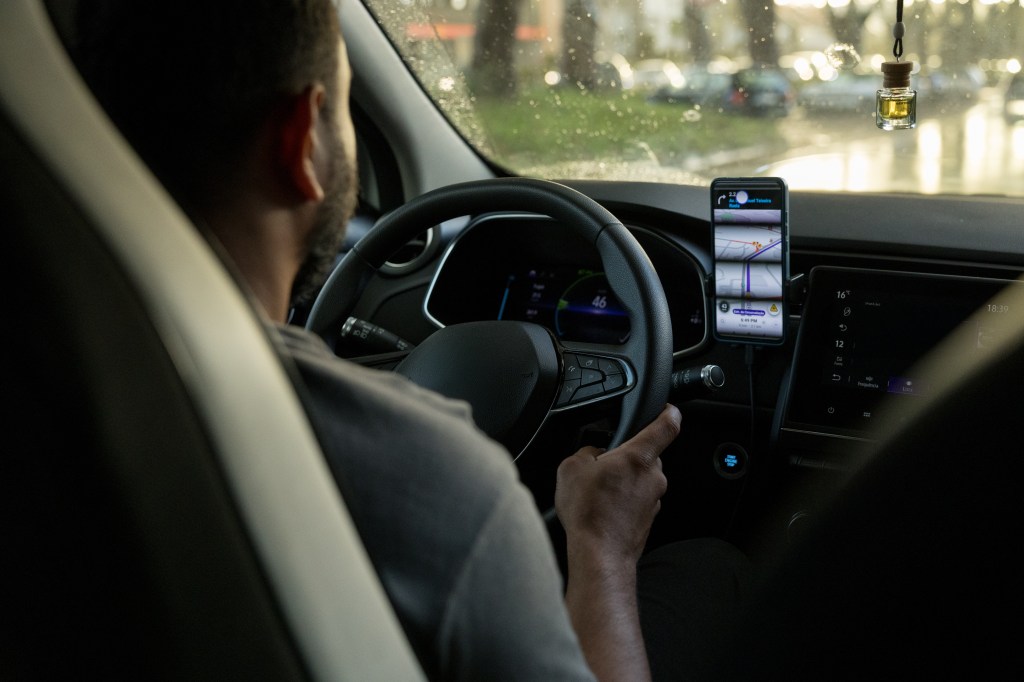 person at the wheel of a car with a cell phone on the dashboard