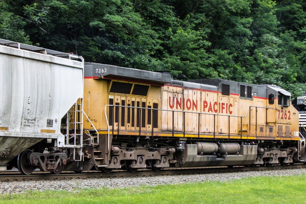 A Union Pacific freight train, number 7262, on tracks with forested mountains in the background.