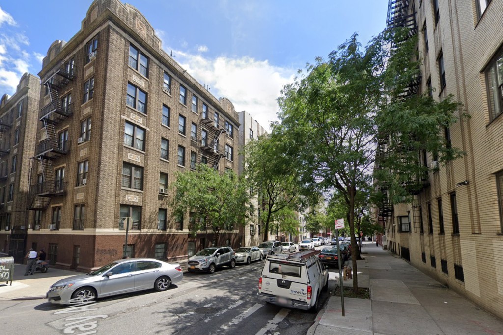 View of a city street with parked cars and multi-story brick buildings lining both sides.