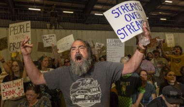 A passionate protestor shouts with a sign demanding water rights amid a crowd holding various protest signs.
