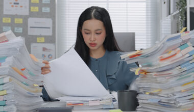 Asian Business woman working busy with massive stacks of documents check and review preparation data report or organizing paperwork workplace stress and administrative overload