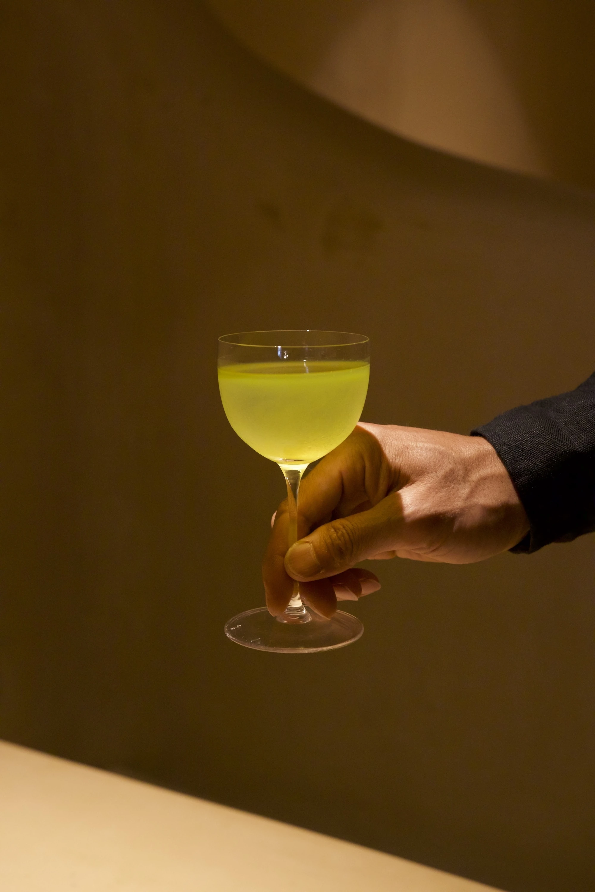 A person holding a green drink in a coupe glass