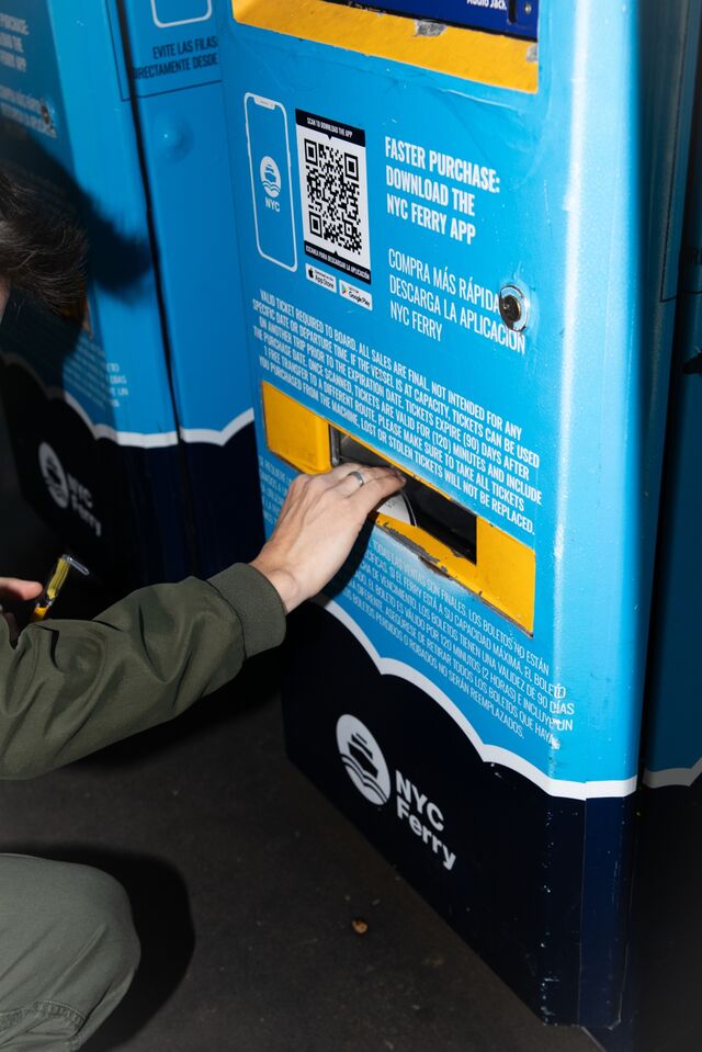 a hand reaching into blue ferry ticket machine