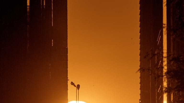 The setting sun is framed between buildings during Manhattanhenge along...