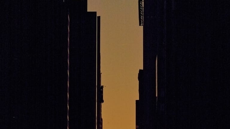 The setting sun is framed between buildings during Manhattanhenge along...