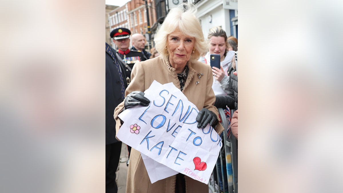 Queen Camilla holding a sign outdoors at a farmers market in Shrewsbury England