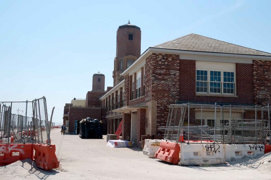 Construction underway at the historic Jacob Riis Bathhouse, featuring brick buildings and two towers, with fencing and building materials in the foreground.