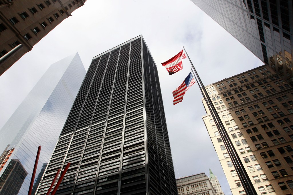 A low-angle photo looking up at tall buildings surrounding One Liberty Plaza in New York City, with an American flag and BBH flag flying between them.