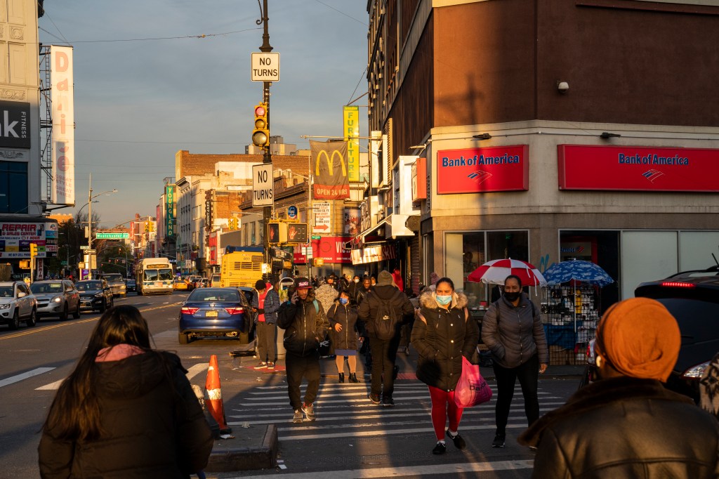 Pedestrians crossing a street in the Bronx with a Bank of America and McDonald's in the background.