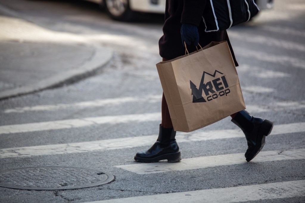 A shopper carries an REI bag while crossing a street.