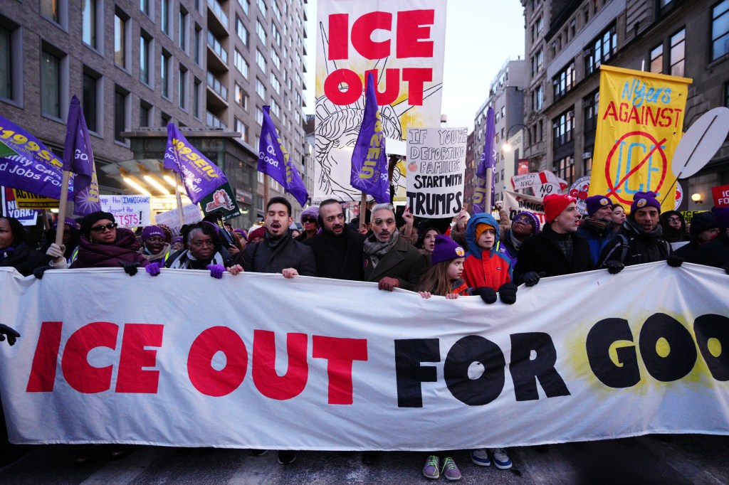 Protesters hold a large white banner that reads "ICE OUT FOR GOOD" in red and black letters.