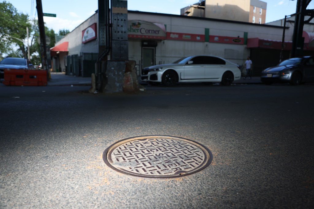 A manhole cover on a city street, with cars and a building in the background.
