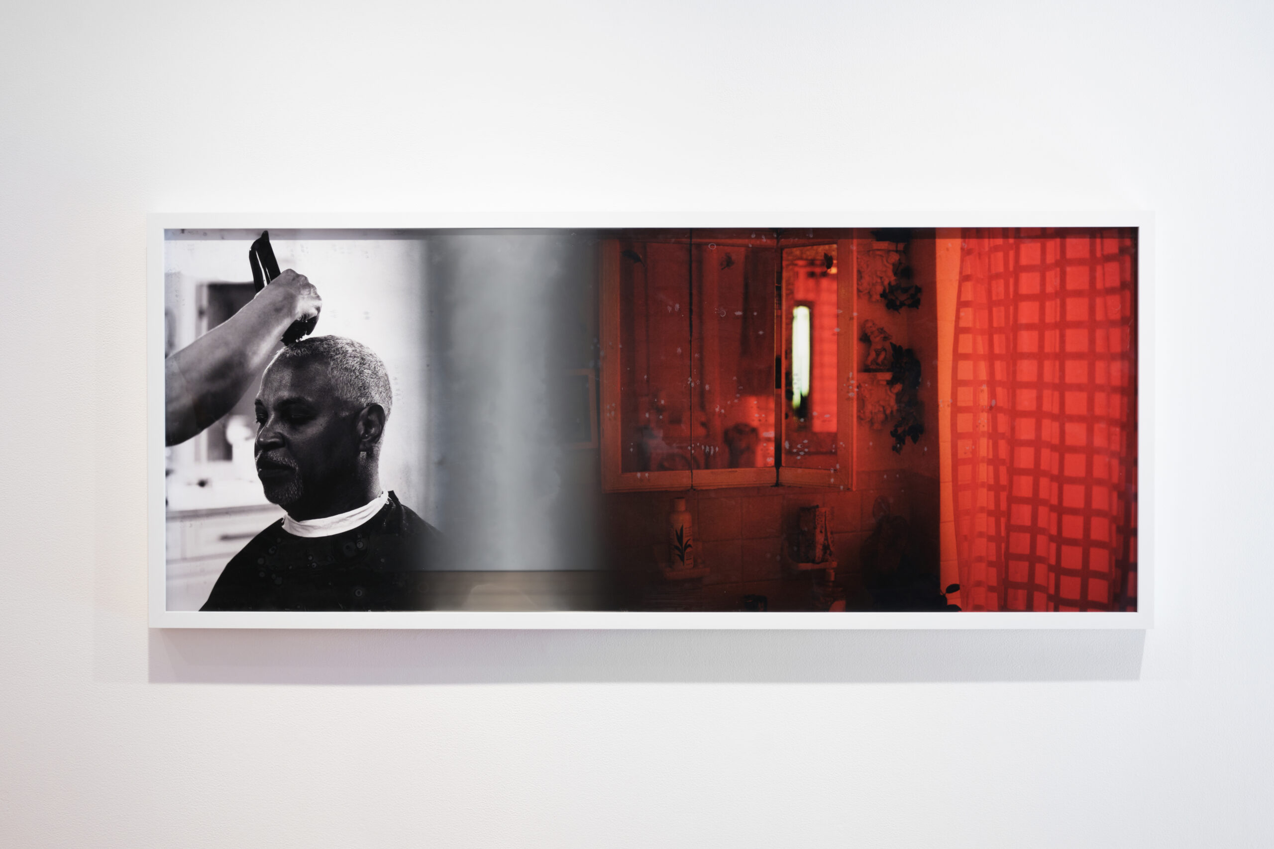 In a rectangular frame, an image of an elder having his hair buzzed is juxtaposed with an image of a bathroom cabinet and shower curtain illuminated in red light.