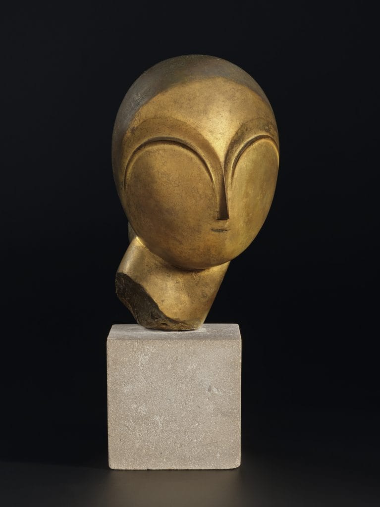 Abstract bronze sculpture of a stylized human head with smooth, rounded features and closed almond-shaped eyes carved in shallow relief. The head tilts slightly on a rough-cut base and is displayed on a light stone pedestal against a black background.