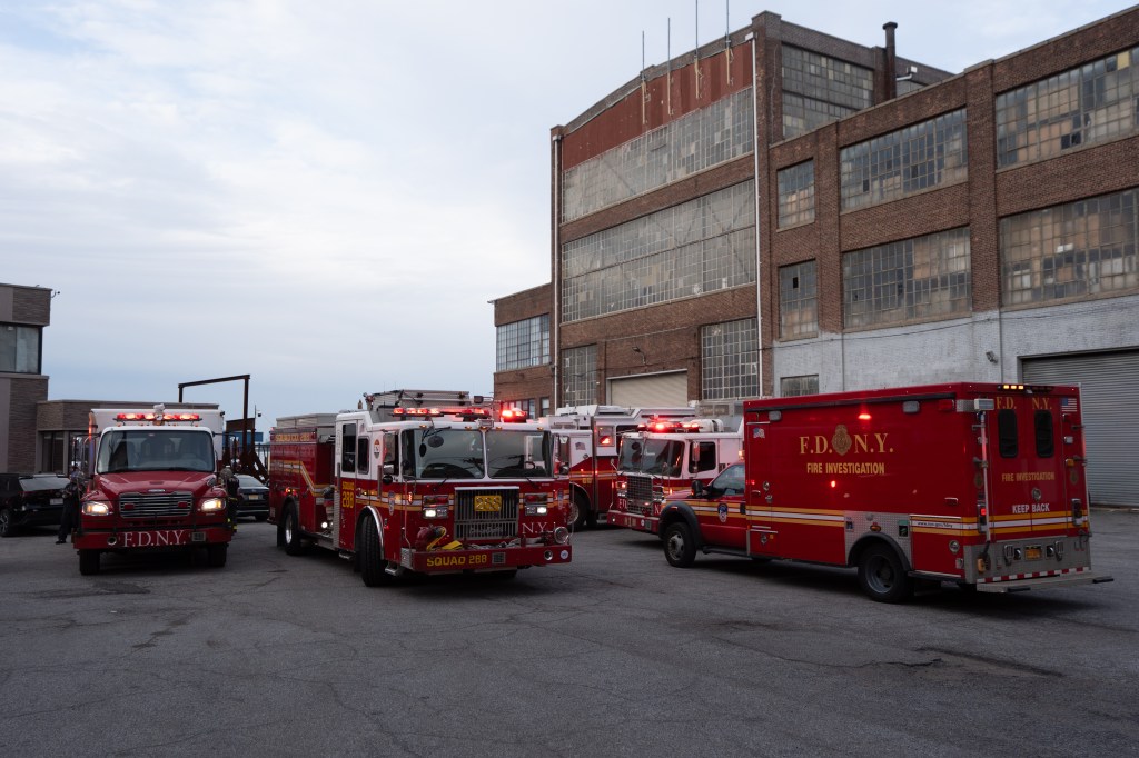 Firetrucks and a fire investigation vehicle gathered outside a large brick building.