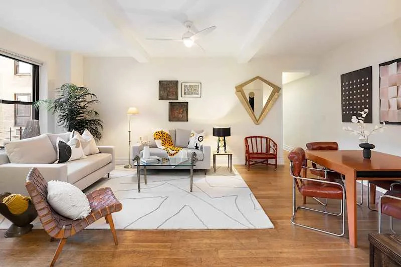 Bright living room with a light sofa, wooden dining table, and decorative art pieces on the walls.