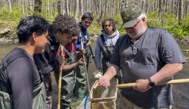 Studens and an instructor stand near river to release trout raised in the classroom
