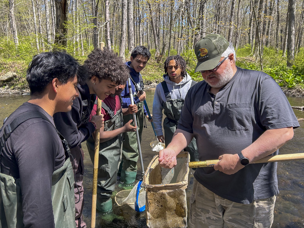 Studens and an instructor stand near river to release trout raised in the classroom