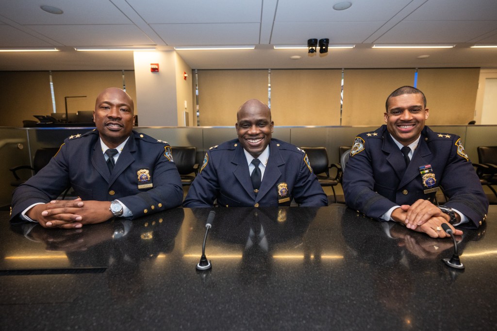 Three uniformed Black police officers smiling at a conference table.