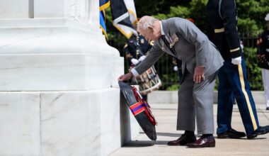 A man wearing a suit bends over to lay a wreath at the base of a marble memorial.