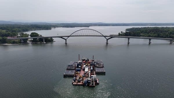 A barge on a lake in front of a bridge.