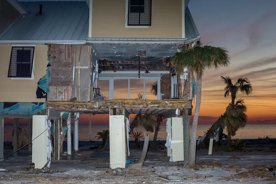 Partially destroyed elevated beach house with exposed interior and palm trees at sunset by the ocean