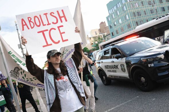 A man holds a sign that reads ''Abolish ICE'' as Newark police drive alongside him during an International Workers' Day rally an