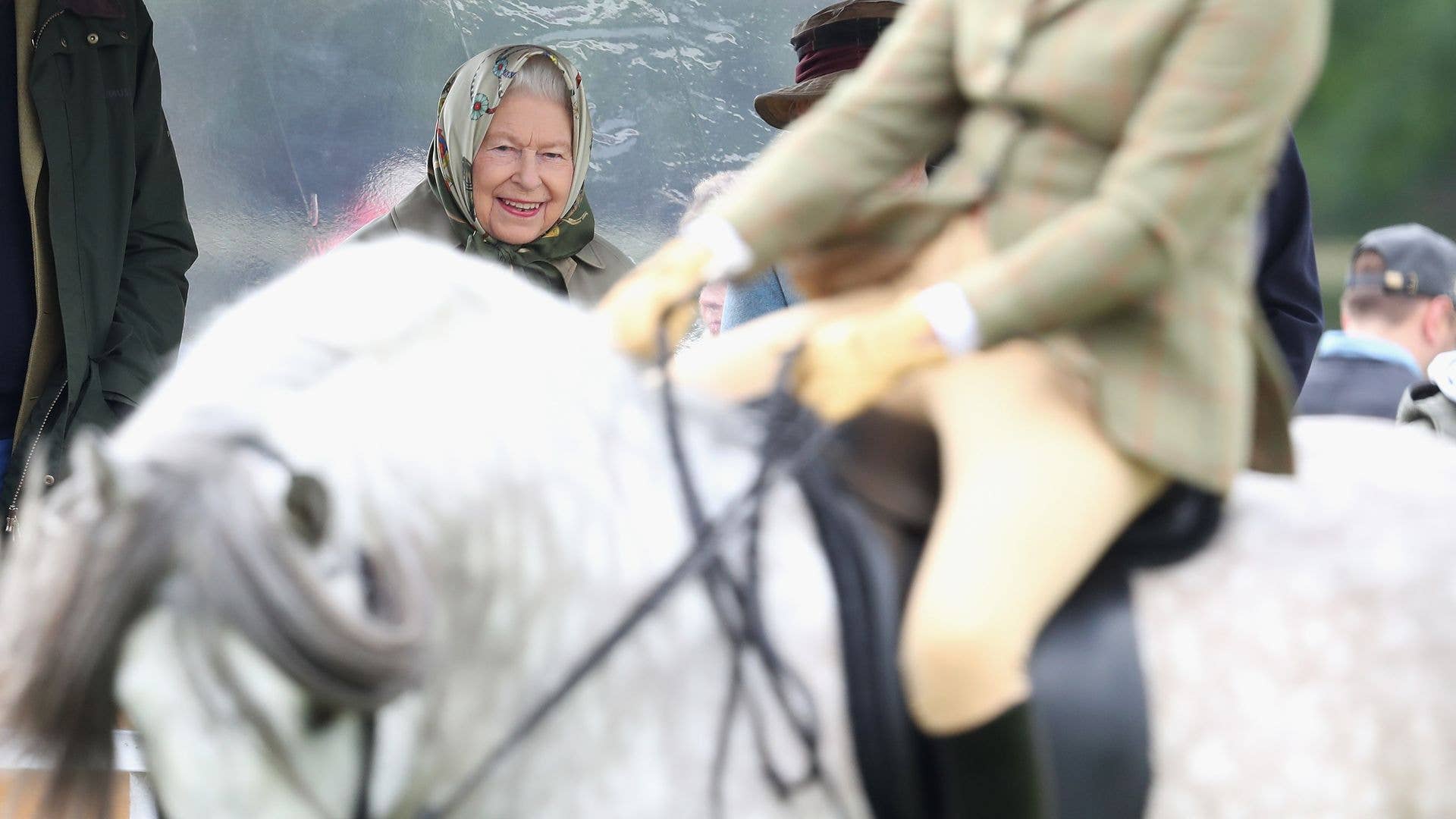The Queen smiling as she looks at a white horse