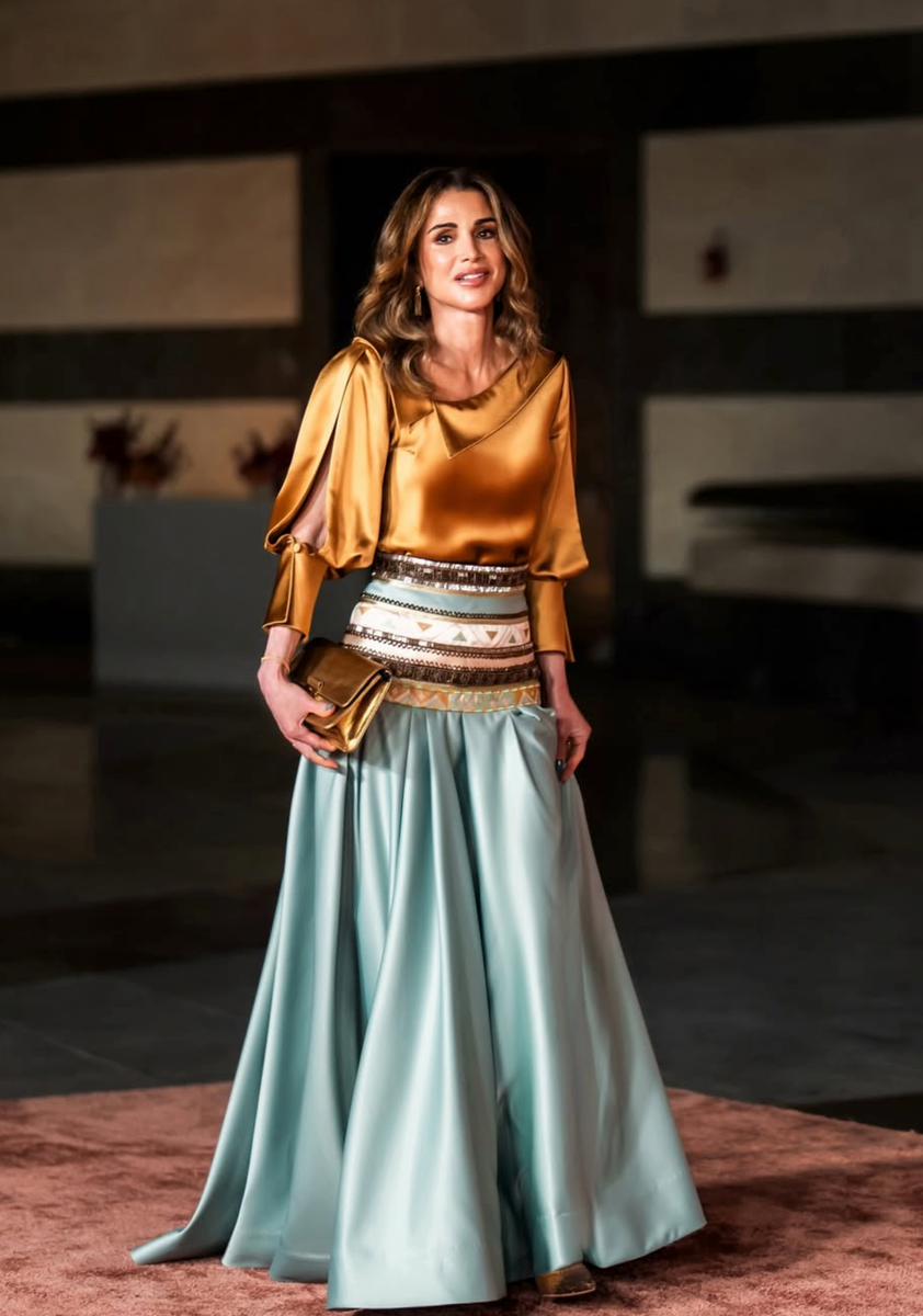 Queen Rania wore a copper-toned top with an asymmetric camisole neckline, puffed sleeves with slit details and fitted cuffs, paired with a spectacular floor-length skirt in aquamarine. 