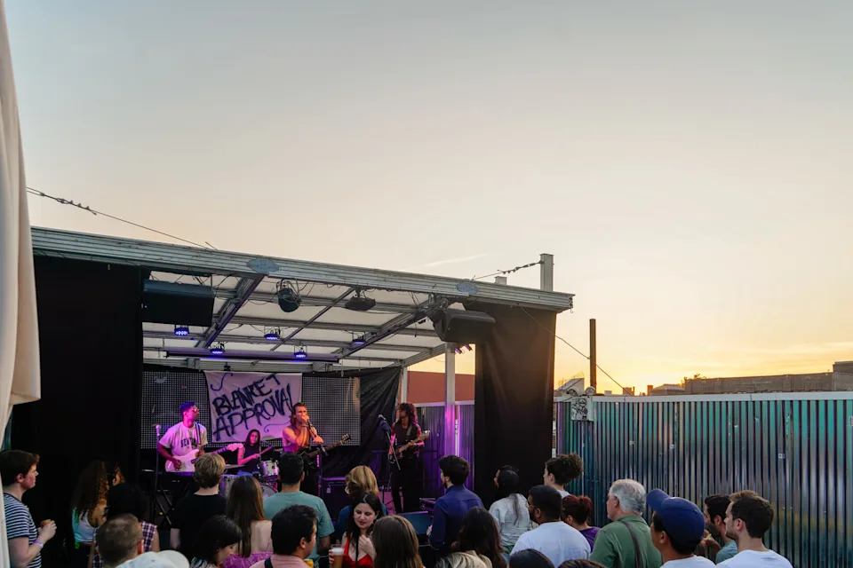 A band plays in front of a crowd on a rooftop at sunset