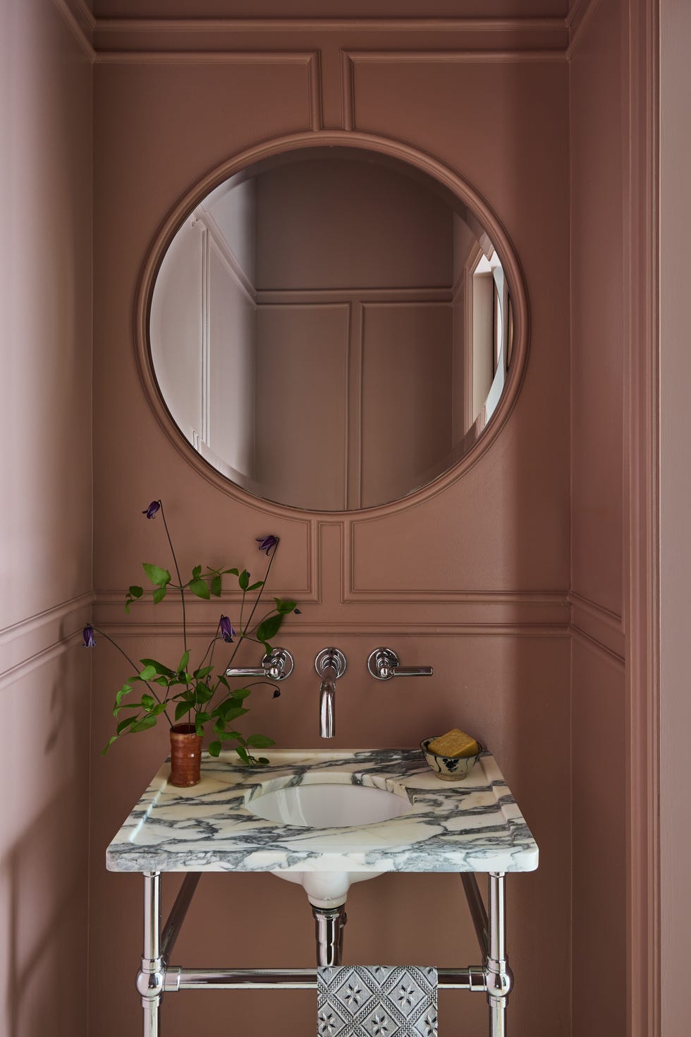 Elegant bathroom sink setup with a round mirror and decorative plant.
