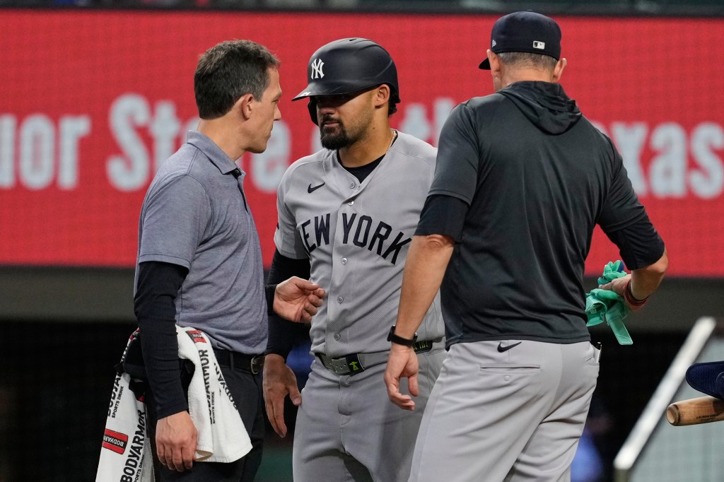 New York Yankees' Jasson Dominguez, center, talks with a team trainer as manager Aaron Boone, right, looks on after Dominguez was hit by a pitch in the fourth inning of a baseball game against the Texas Rangers Wednesday, April 29, 2026, in Arlington, Texas. 