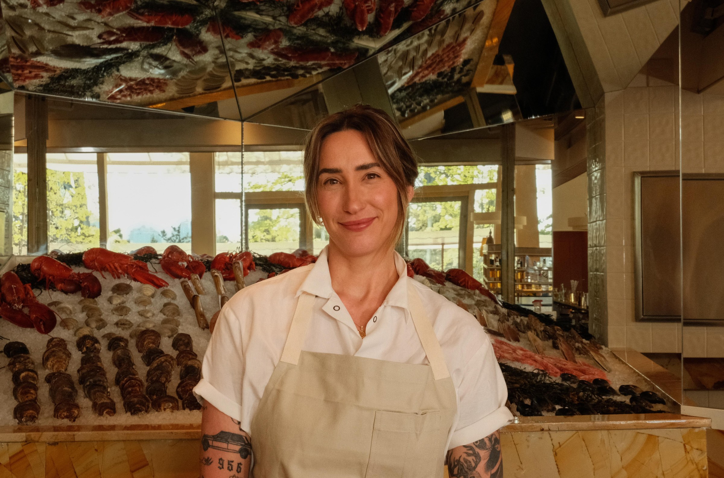A woman in a chef coat and apron standing in front of a raw bar.