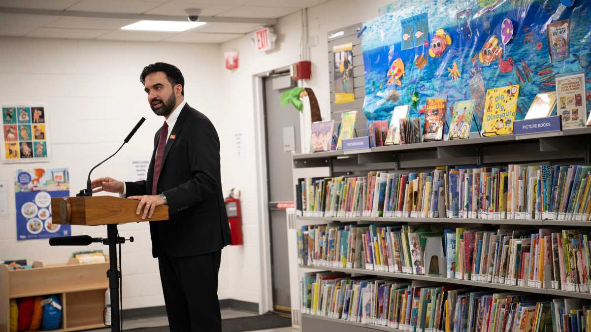 mayor mamdani speaking at podium in front of book shelves full of books