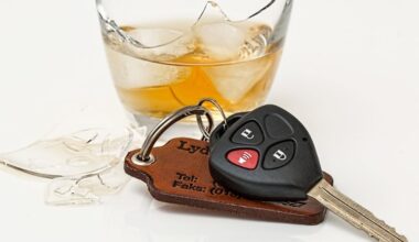 A car key with a leather fob lies next to a broken glass of whiskey with ice, symbolizing impaired driving.