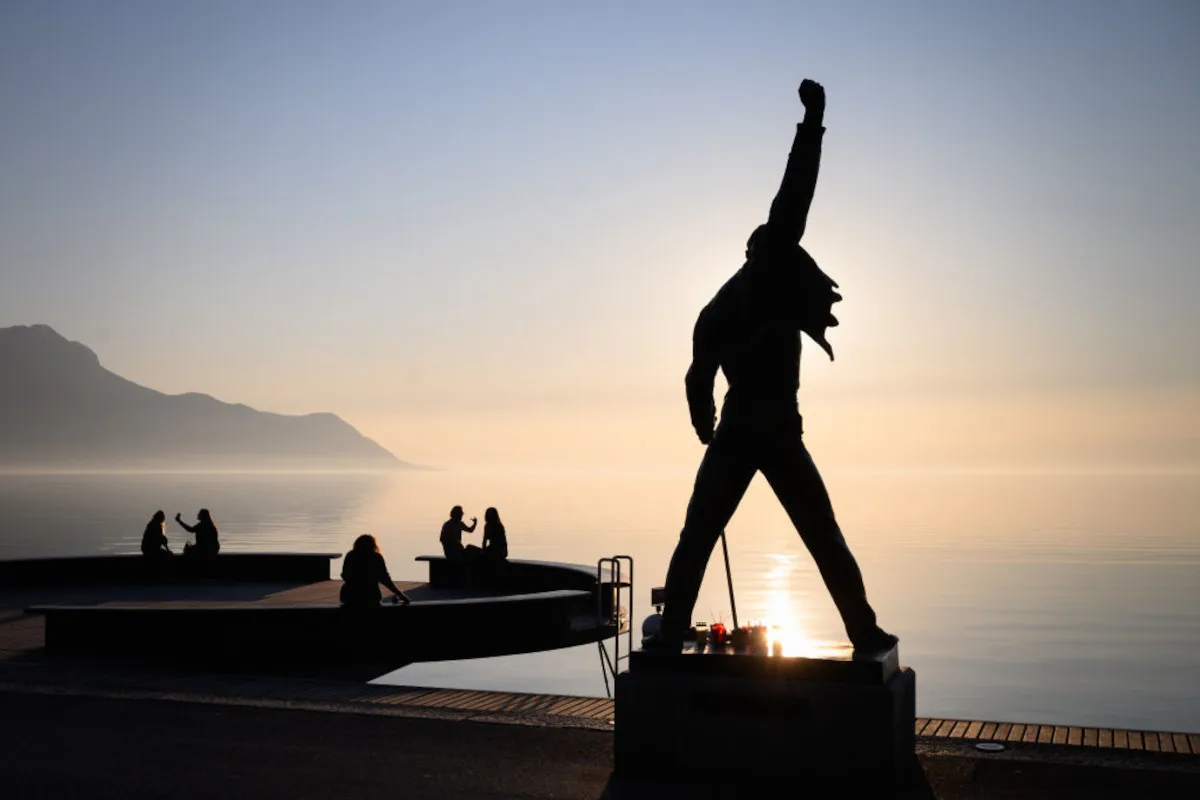 People sit on a bench at sunset close to a statue of the rock band Queen's late singer Freddie Mercury, in silhouette, erected on the shores of Lake Geneva, 2020